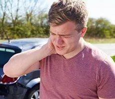 A man holding his neck in pain near an accident.