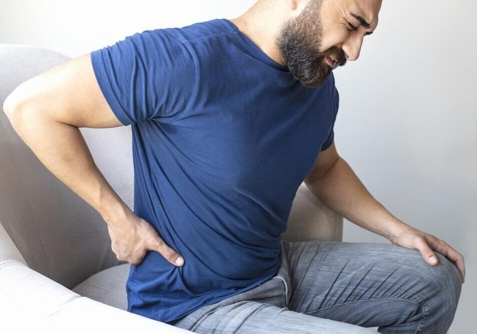 A man with back pain sitting on a chair.